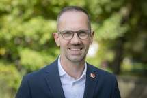 Portrait von Bürgermeister Ansgar Mertens in Hemd und Sakko vor grünen Bäumen.