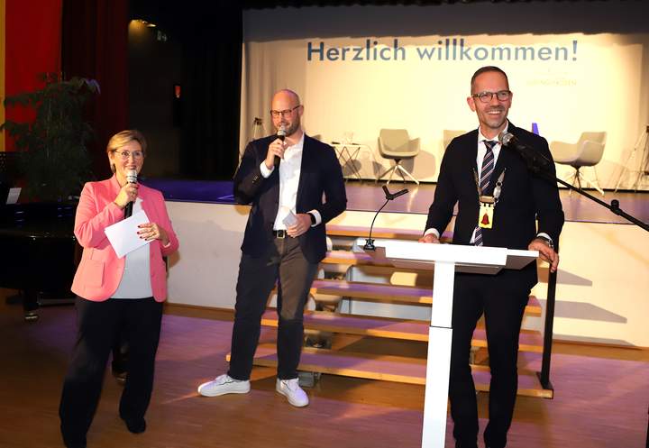 Bürgermeister Ansgar Mertens steht nach seiner Rede am Pult und das Moderatorenteam, Dagmar Stein und Torsten Voß, leiten das Abendprogramm ein.